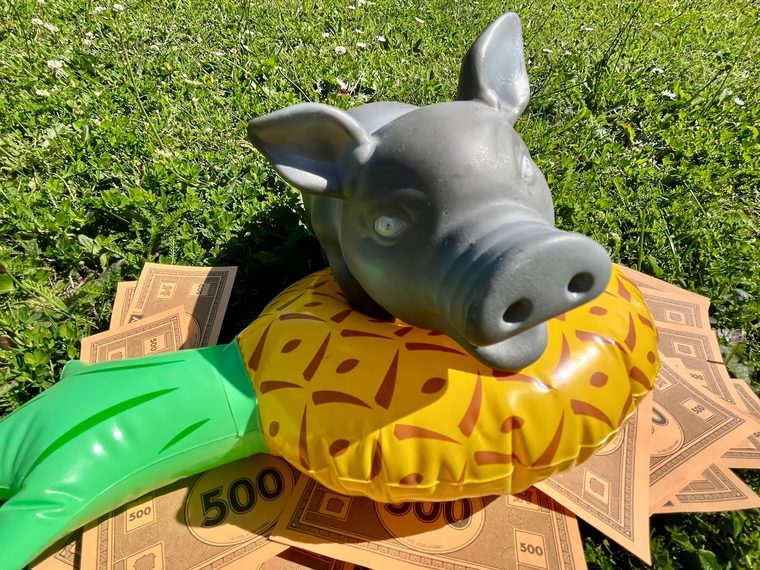 Pendule, tirelire cochon en céramique posée sur des billets de Monopoly